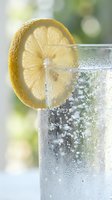 Refreshing lemon slice garnishing a fizzy carbonated beverage in a condensation-covered glass against a soft blurred green outdoor background.