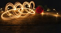 Golden light trails creating heart shapes with red rose on wooden surface for romantic Valentine's Day celebration and love concept photography.
