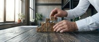 Businessman building wooden block tower with star symbols on rustic desk in modern office environment representing growth strategy and success.