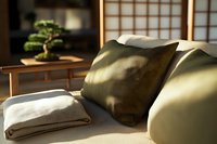 Cozy minimalist sofa corner with olive green pillows and folded blanket in sunlit room with Japanese shoji screen and bonsai tree creating peaceful atmosphere.