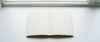 Open blank notebook with aged moss-covered spine displayed on white surface near window, suitable for journaling, writing, and creative projects.
