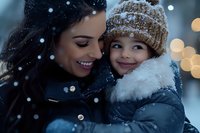 Mother and young child embracing outdoors during snowfall, wearing winter clothing. Warm family moment with holiday bokeh lights in background, suitable for seasonal campaigns.