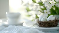 Delicate spring composition with speckled eggs in small nest on white plate, fresh cherry blossoms and soft morning light creating dreamy atmosphere.