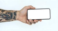 Tattooed hand holding blank smartphone with white screen isolated on white background for mockup and app presentation purposes.