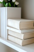 Stack of white hardcover books on shelf with green plant in background, creating minimalist home decor aesthetic for modern interior styling.