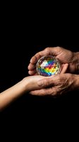 Two hands holding a colorful crystal sphere with rainbow prism reflections against black background. Represents unity, diversity, hope and shared vision for design and editorial use.
