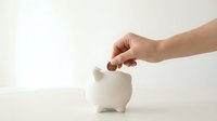 Hand inserting coin into white ceramic piggy bank on clean background for savings and financial planning concepts.