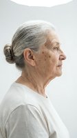 Senior woman with gray hair in profile view wearing casual white t-shirt against neutral background. Suitable for healthcare, aging, wellness and lifestyle editorial use.