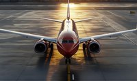 Commercial passenger aircraft on airport runway at sunset with golden light reflecting off fuselage, front view showing cockpit and engines.