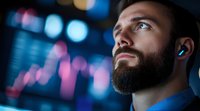 Bearded male trader wearing earbuds monitors stock market data on digital display. Financial professional analyzes rising pink and blue charts for investment decisions and trading strategy.