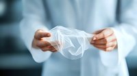Hands in white medical coat stretching transparent protective glove, showing quality control and safety measures in healthcare environment. Medical equipment testing.