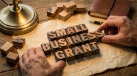 Small business grant concept with wooden letterpress blocks on rustic paper, male hands arranging text, vintage lamp and notebook on wooden table.