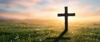 Wooden cross silhouette in green meadow at golden sunrise with soft clouds, spiritual faith symbol for Easter, Christianity and religious worship concepts.