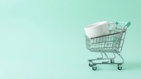 Miniature shopping cart filled with white box on pastel mint background, representing retail, e-commerce, and online shopping concepts for commercial use.