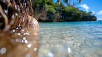 Young woman enjoying crystal clear tropical water with blurred bokeh water drops and limestone cliffs in background, summer vacation concept.
