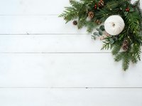 Festive evergreen garland with pinecones and cream candle arranged on white wooden surface, ideal for holiday decorating, seasonal marketing, and Christmas design projects.