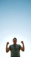 Excited male with dark hair and olive skin tone wearing olive green t-shirt celebrating with fists raised against clear blue sky, expressing joy and success for motivational and achievement concepts.