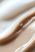 Single water droplet on smooth brown and white wavy surface creates minimalist abstract composition with gentle curves and soft light reflections.
