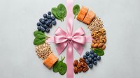 Healthy food gift wreath with pink ribbon, fresh blueberries, salmon, nuts and spinach leaves arranged in festive circle for wellness celebration.