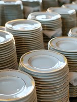 Stacks of elegant white porcelain dinner plates with delicate gold trim arranged in neat piles, creating a clean and sophisticated dining service display.