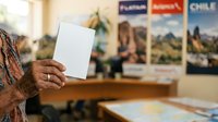 Mature woman holding blank white card in travel agency office with destination posters on wall, planning vacation.
