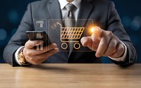 Businessman in suit touching glowing virtual shopping cart icon while holding smartphone, digital e-commerce and online retail technology concept.