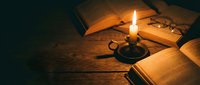 Vintage candle illuminating open books on wooden table creating warm atmospheric lighting for reading and study sessions.