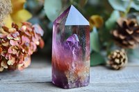 Mystical fluorite crystal point with purple and orange hues on wooden surface, surrounded by dried hydrangea flowers and pine cones, spiritual healing setup.