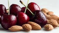 Fresh dark cherries with water droplets alongside raw almonds on white background, showcasing natural ingredients for healthy snacking or dessert preparation.