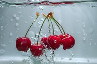 Fresh red cherries with stems splashing into clear water with bubbles and dynamic water movement, captured in high-speed photography for food and beverage advertising.