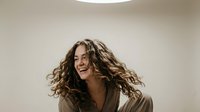 Young woman with curly hair laughing joyfully in motion, expressing happiness and positive emotions for lifestyle and wellness content.