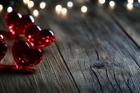 Red heart-shaped ornaments on rustic wooden surface with warm bokeh lights creating romantic Valentine's Day atmosphere for greeting cards and decorations.