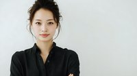 Young Asian woman with natural makeup and hair in updo wearing black shirt against white background, conveying confidence and professionalism.