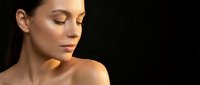 Young woman with glowing skin and closed eyes in warm lighting against dark background for beauty and skincare concepts.