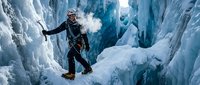 Male mountaineer climbing frozen waterfall with ice axes in dramatic blue ice canyon during winter expedition.