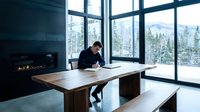 Professional businessman working at wooden desk in modern office with mountain forest view and fireplace during winter season.