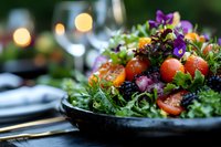 Fresh garden salad with cherry tomatoes, mixed greens, and edible purple flowers served on dark plate with romantic dinner setting and soft bokeh lights.