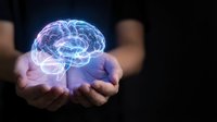 Glowing digital brain hologram floating above cupped hands against dark background representing artificial intelligence, neuroscience and mental health concepts.