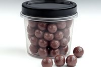 Round chocolate candies in clear plastic container with black lid on white background, isolated confectionery product for packaging and food marketing.