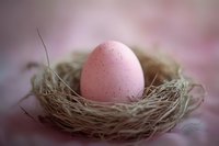 Pink speckled egg resting in natural straw nest against soft blurred background, creating gentle Easter composition with delicate lighting and shallow depth of field.