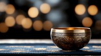 Ornate metal singing bowl with intricate engravings on blue textile against blurred golden bokeh background for meditation and sound healing practices.