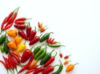 Fresh red, orange, and green chili peppers arranged on white background, isolated for culinary, cooking, and food design projects.