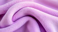 Soft pink fleece fabric with gentle folds and waves creating abstract texture pattern, close-up view showing plush material surface detail for textile design background.