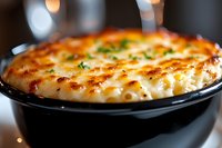 Creamy baked mac and cheese casserole topped with melted golden cheese and fresh herbs, served in black cast iron skillet with crispy browned edges.