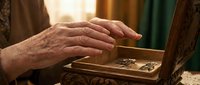 Elderly hands gently touching vintage wooden jewelry box in warm sunlight, showcasing craftsmanship and sentimental memories in cozy home interior setting.