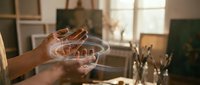 Artist hands holding glass palette in sunlit studio workspace for creative painting and art projects.