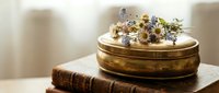 Vintage brass jewelry box with dried flowers on antique leather book creates elegant still life composition for home decor and luxury lifestyle concepts.