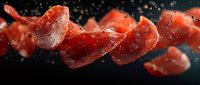 Sliced red pepperoni or salami pieces suspended in mid-air with water droplets against dark background, suitable for food advertising and culinary designs.