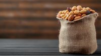 Mixed nuts and dried fruits in rustic burlap sack on dark wooden background, selective focus with copy space for healthy snack concept.