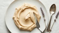 Creamy beige whipped dessert topping swirled on white plate with vintage spoon and dried lavender sprigs, overhead flat lay composition for culinary and baking content.